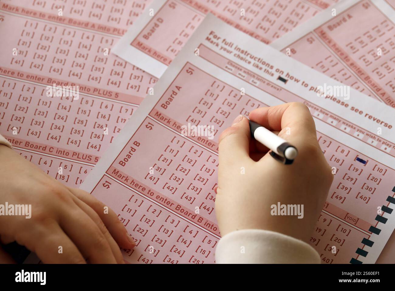 Ein Lotterielos ausfüllen. Eine junge Frau spielt im Lotto und träumt davon, den Jackpot zu gewinnen. Weibliche Handzeichen auf rotem Lotterielos Stockfoto