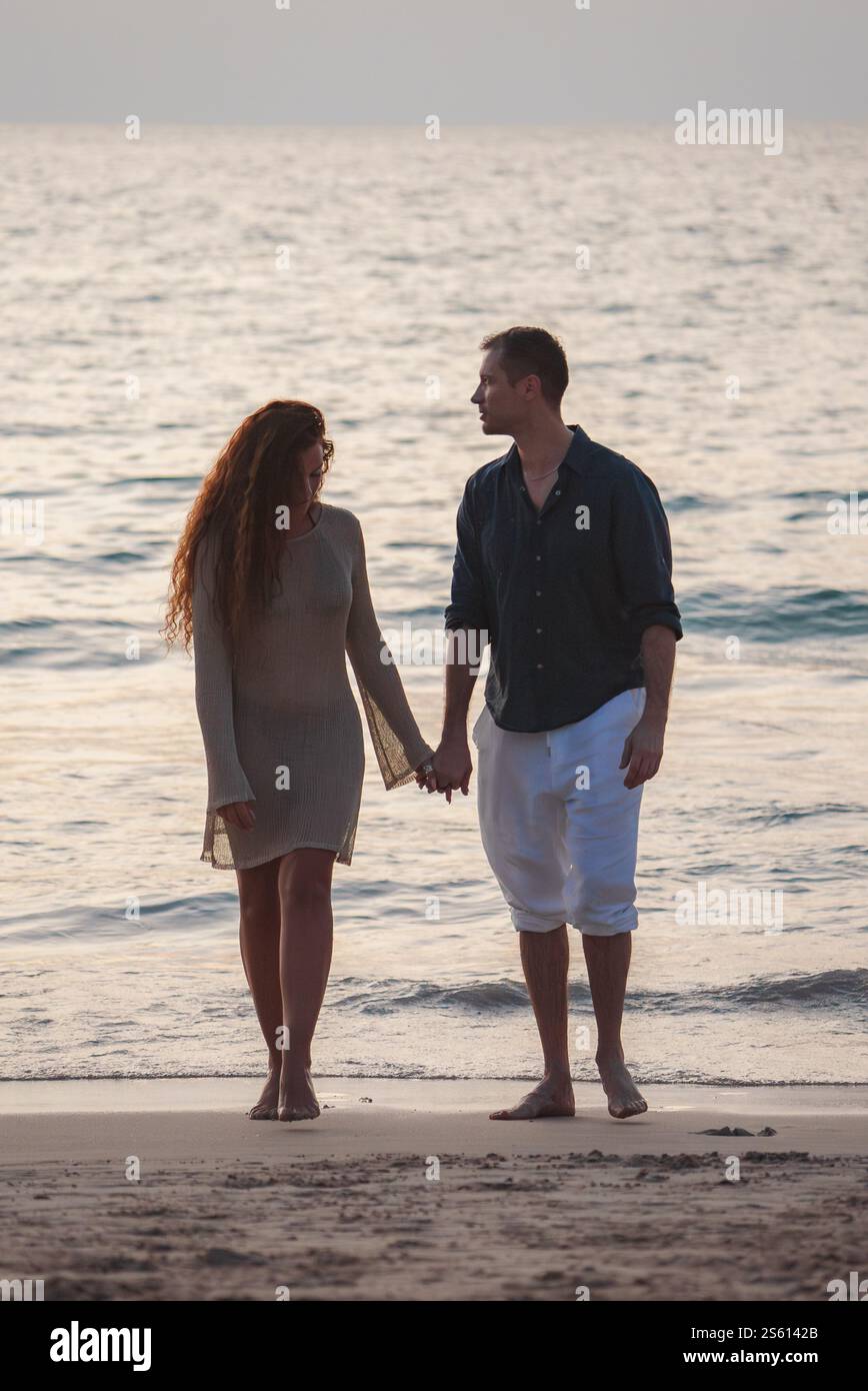 Ein Paar spaziert an einem Sandstrand bei Sonnenuntergang in Phuket, Thailand Stockfoto