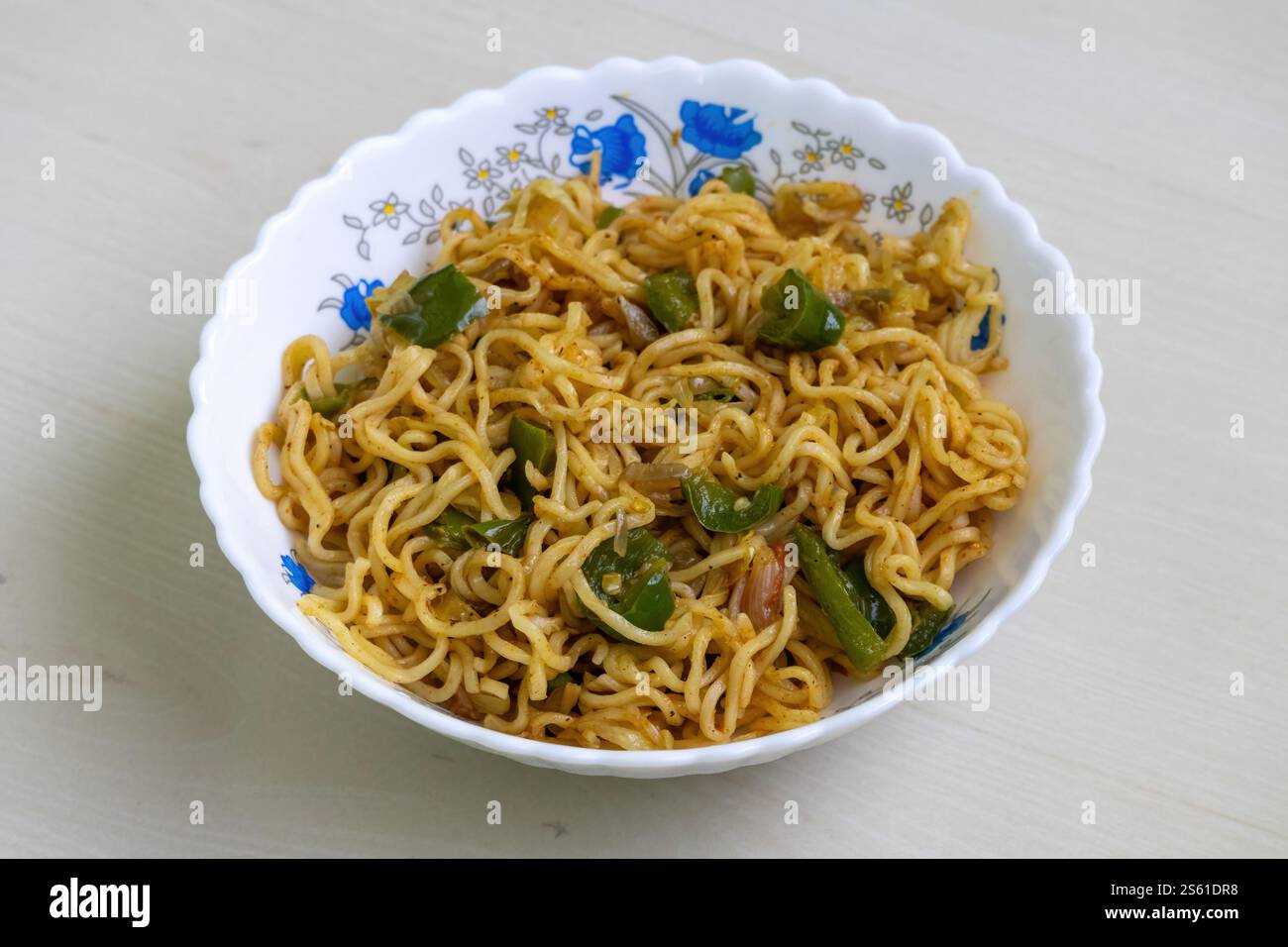 Eine Schüssel mit geschmackvollen hausgemachten Nudeln, gebraten mit lebendigem grünem Paprika, saftigen Tomaten und scharfen Chili, serviert in einer weißen Schüssel. Stockfoto