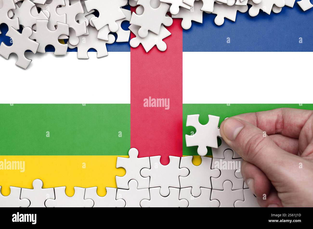 Die Flagge der Zentralafrikanischen Republik ist auf einem Tisch abgebildet, auf dem die menschliche Hand ein weißes Puzzle faltet. Die Flagge der Zentralafrikanischen Republik ist abgebildet Stockfoto