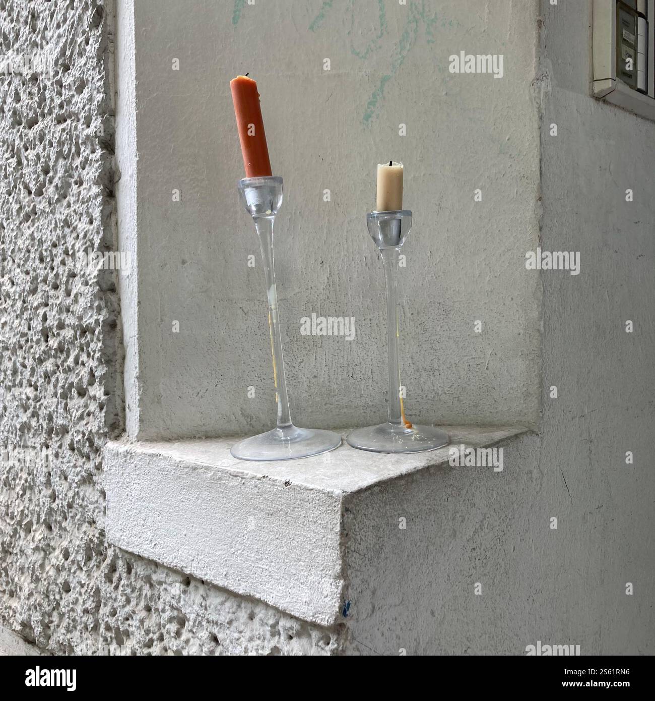 Zwei minimalistische Kerzenhalter mit orangefarbenen und beigefarbenen Kerzen sitzen auf einem Betonvorsprung vor einem strukturierten Hintergrund. - Smartphone-aufgenommenes Stockfoto