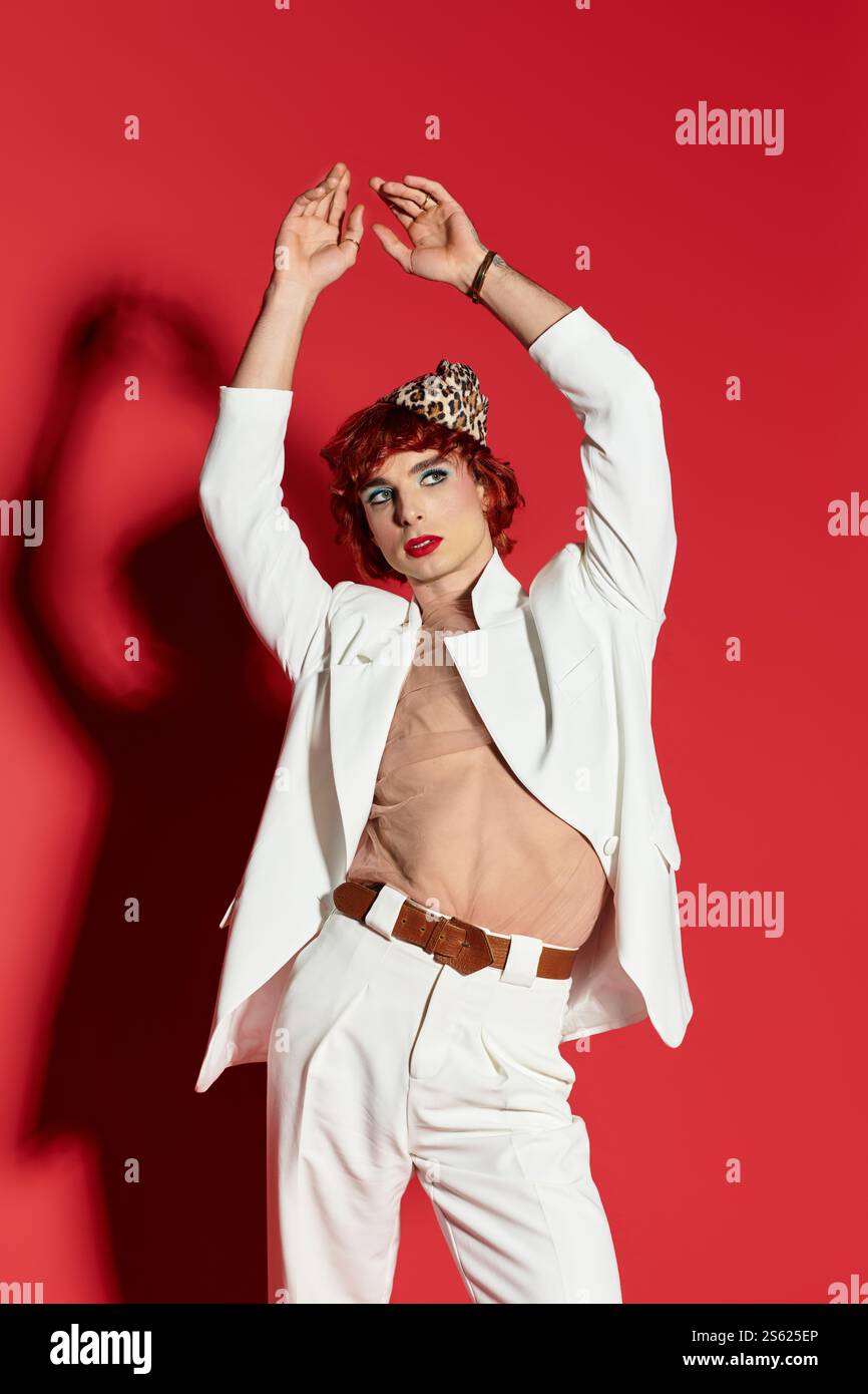 Mit einer auffälligen Pose und einem ausdrucksstarken Stil zeigt ein junger Mann mutige Mode gegen leuchtendes Rot. Stockfoto