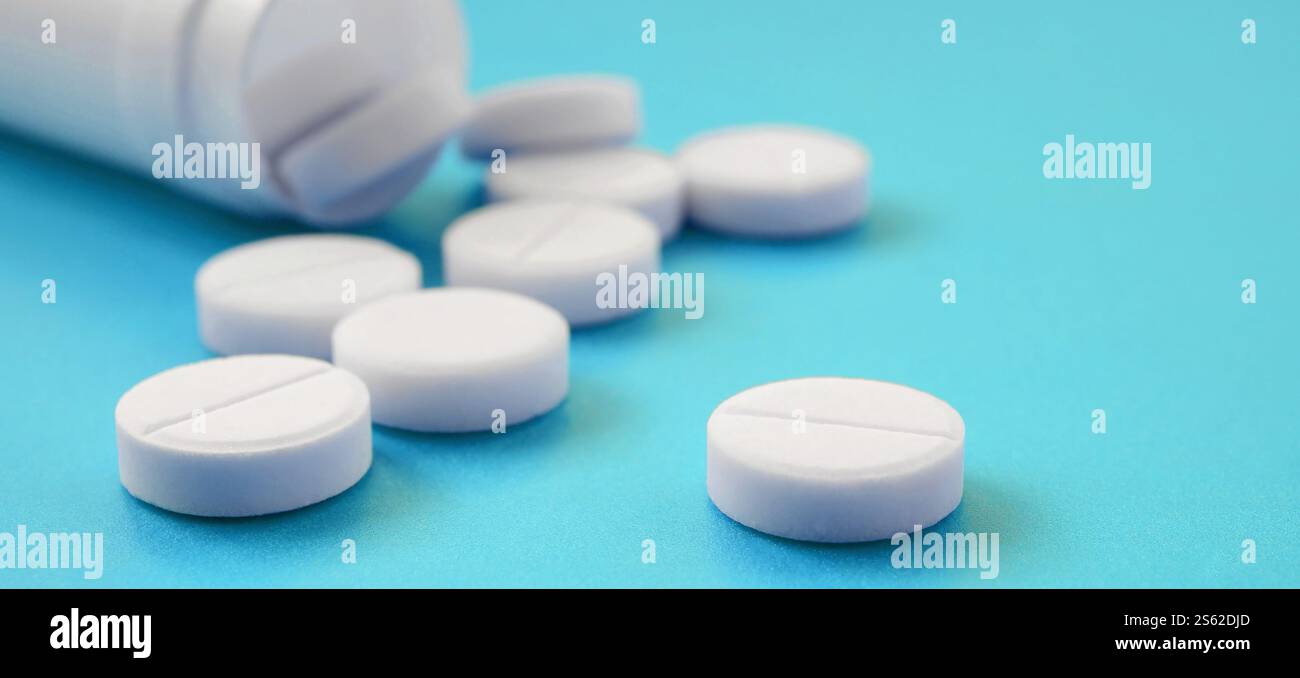 Mehrere weiße Tabletten fallen aus der Kunststoffbehälter auf der blauen Fläche. Hintergrundbild über medizinische und pharmazeutische Themen Stockfoto