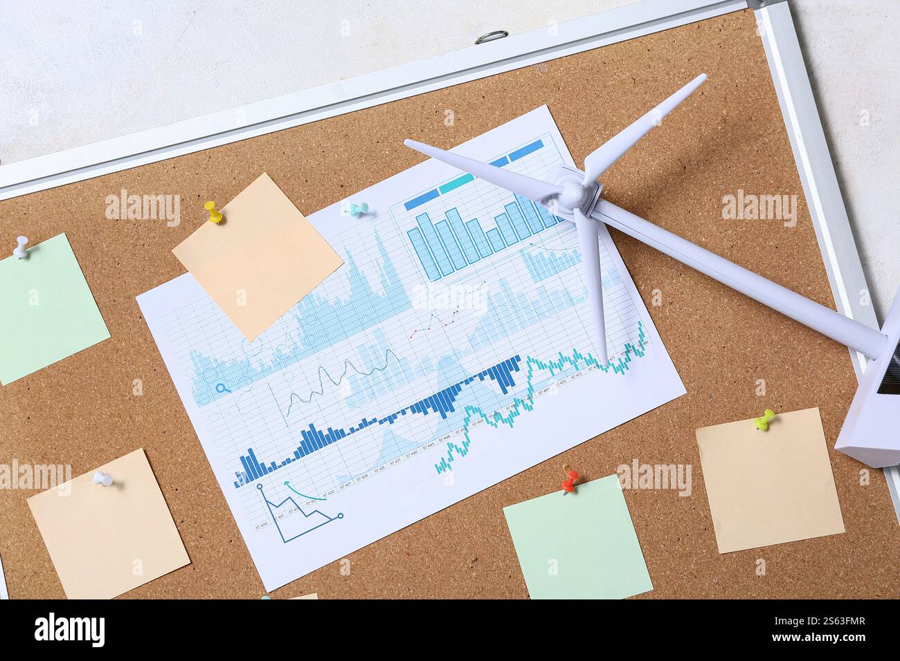 Diagramme mit leeren Haftnotizen und Windkraftanlagenmodell auf Pinnwand. Konzept der grünen Energie Stockfoto