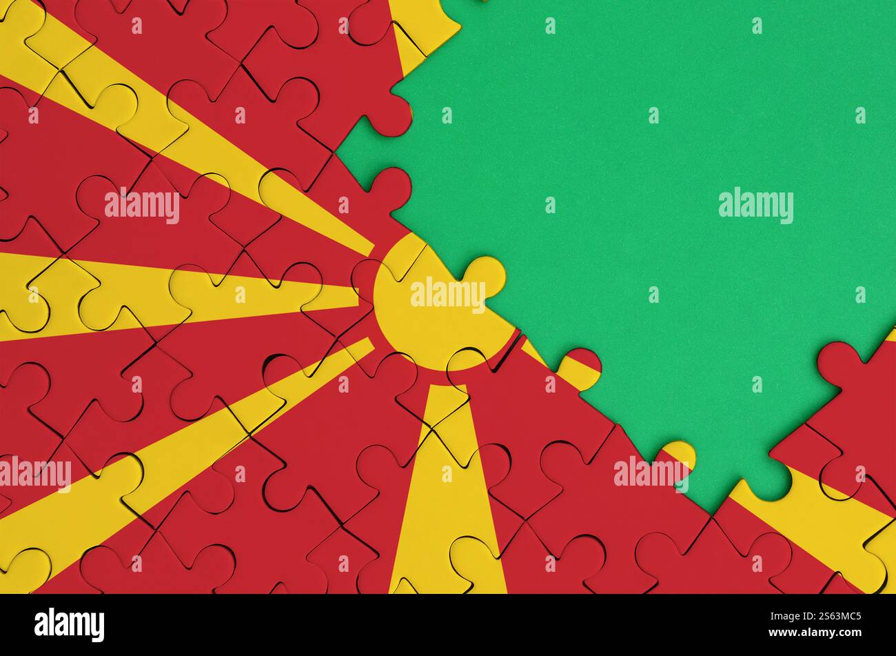 Die Flagge Mazedoniens ist auf einem fertigen Puzzle mit einem freien grünen Kopierraum auf der rechten Seite abgebildet. Mazedonien-Flagge ist auf einem fertig gestellten abgebildet Stockfoto
