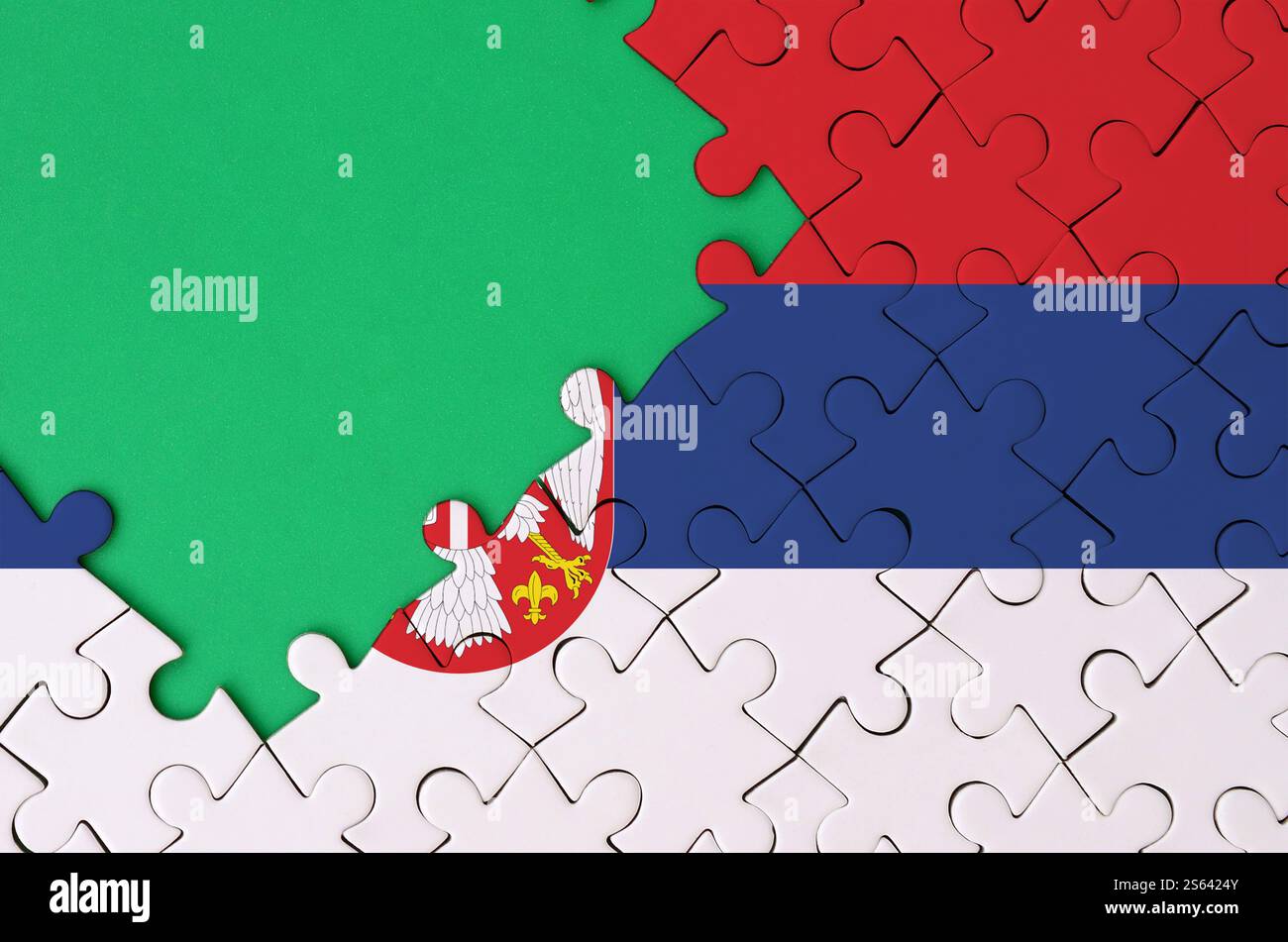 Die serbische Flagge ist auf einem fertigen Puzzle mit freiem grünen Kopierraum auf der linken Seite abgebildet. Die serbische Flagge ist auf einer fertigen Stichsäge abgebildet Stockfoto