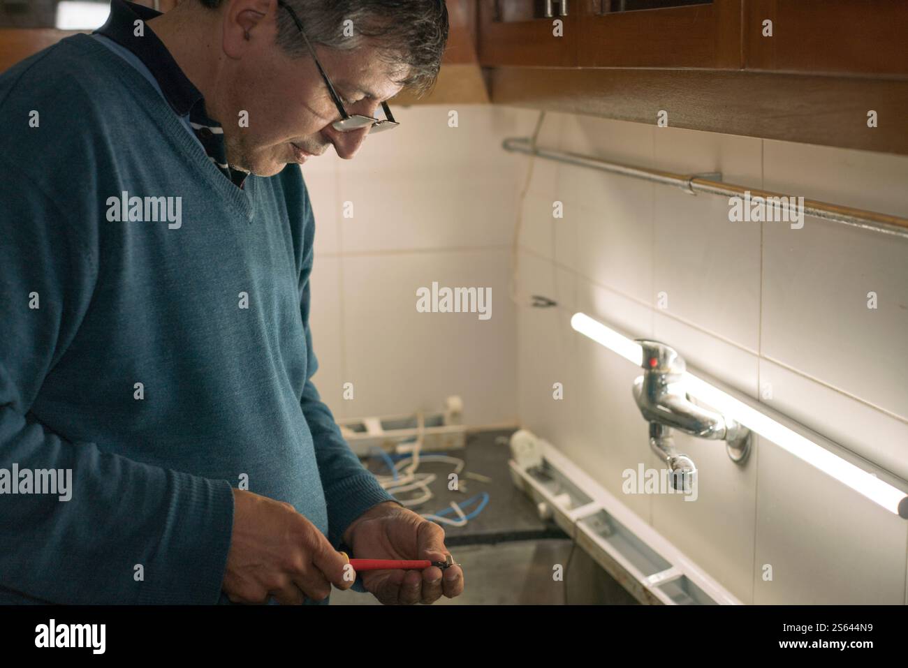 Mann, der sich darauf konzentriert, an der elektrischen Verkabelung einer Küche mit LED-Licht zu arbeiten. Stockfoto