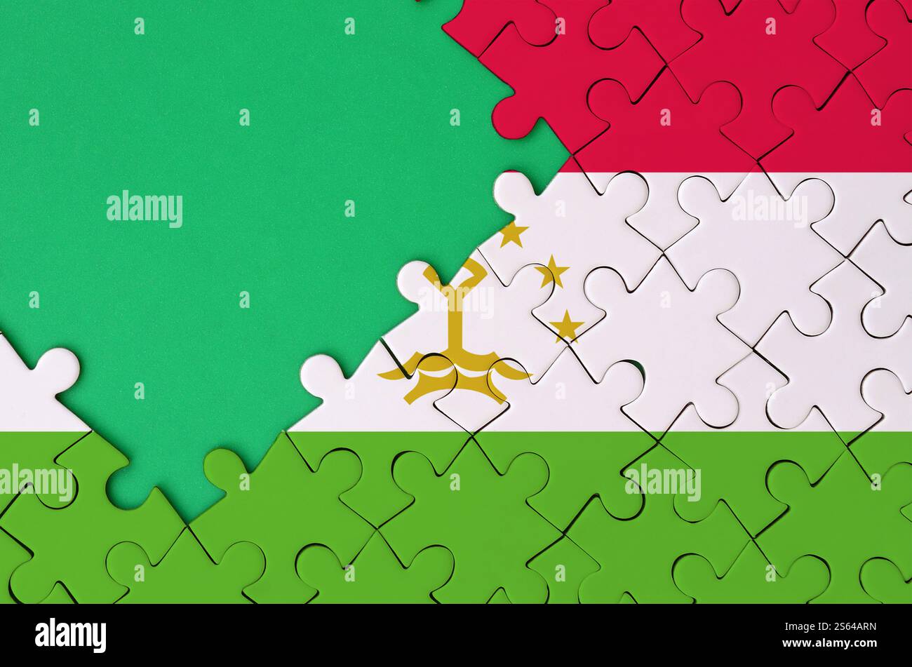 Die Flagge Tadschikistans ist auf einem fertigen Puzzle mit freiem grünen Kopierraum auf der linken Seite abgebildet. Die Flagge Tadschikistans ist auf einem abgeschlossenen abgebildet Stockfoto