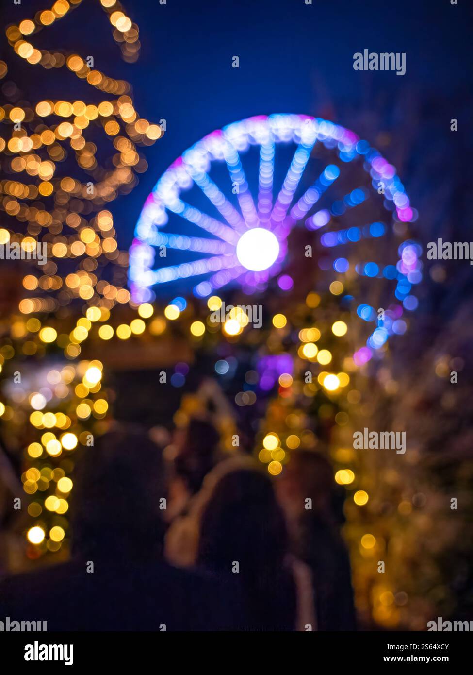 Verschwommenes Bild von Touristen, die vor einem Instagram-würdigen Ort auf dem Weihnachtsmarkt in Colmar Fotos machen, mit einem Riesenrad im Hintergrund Stockfoto