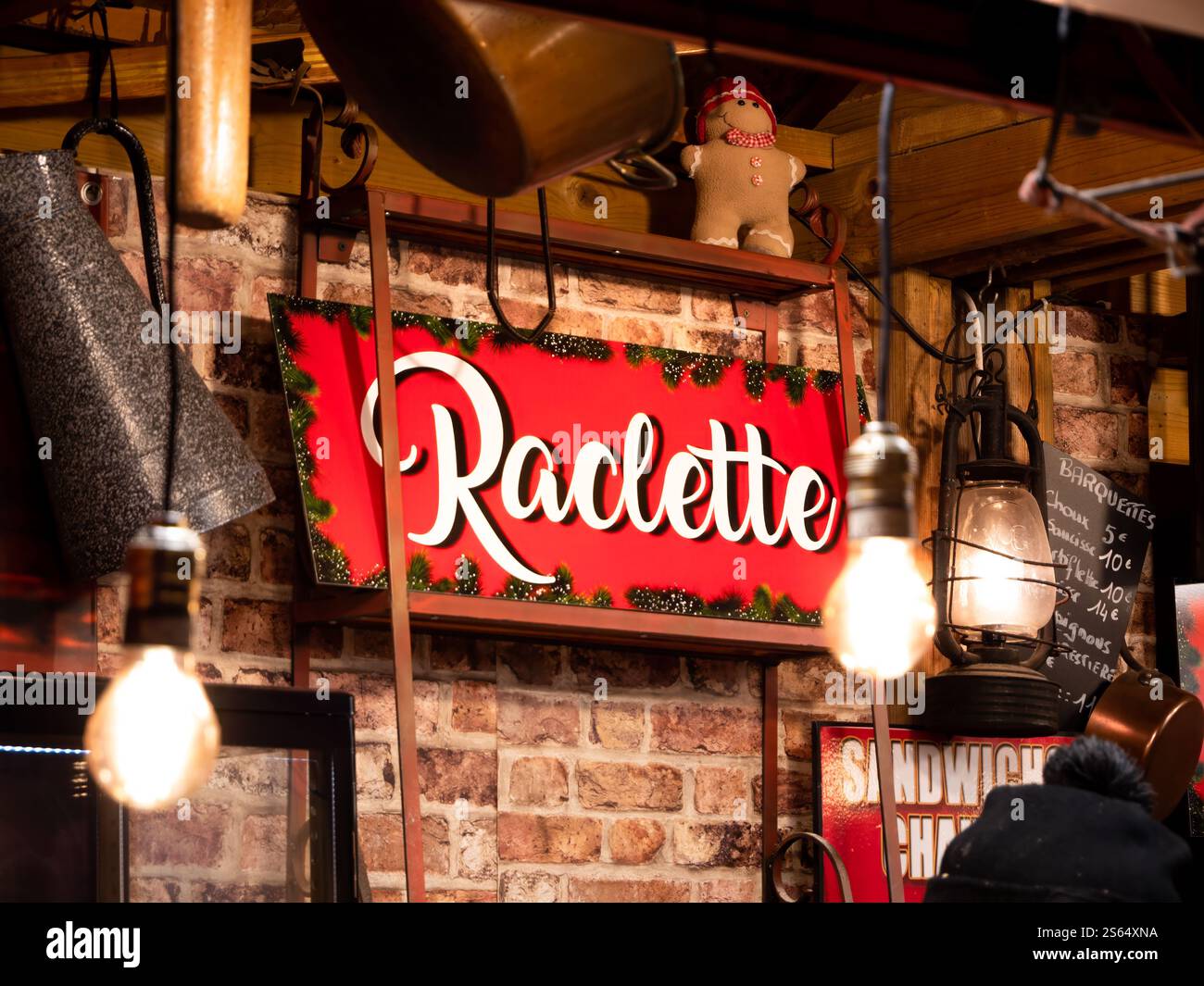 „Raclette“-Schild an einem Weihnachtsmarkt in Colmar, Frankreich. Festliches rotes Schild mit dekorativer Schrift wirbt für Raclette, ein Schweizer Gericht mit geschmolzenem Käse Stockfoto