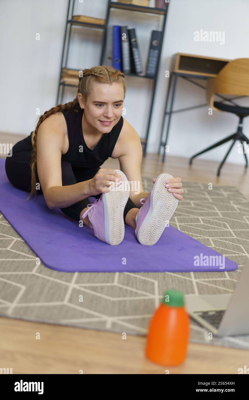 Die Frau macht Yoga auf einer lila Matte. Sie trägt pinkfarbene Schuhe. Eine Flasche Wasser liegt auf dem Boden neben ihr Stockfoto