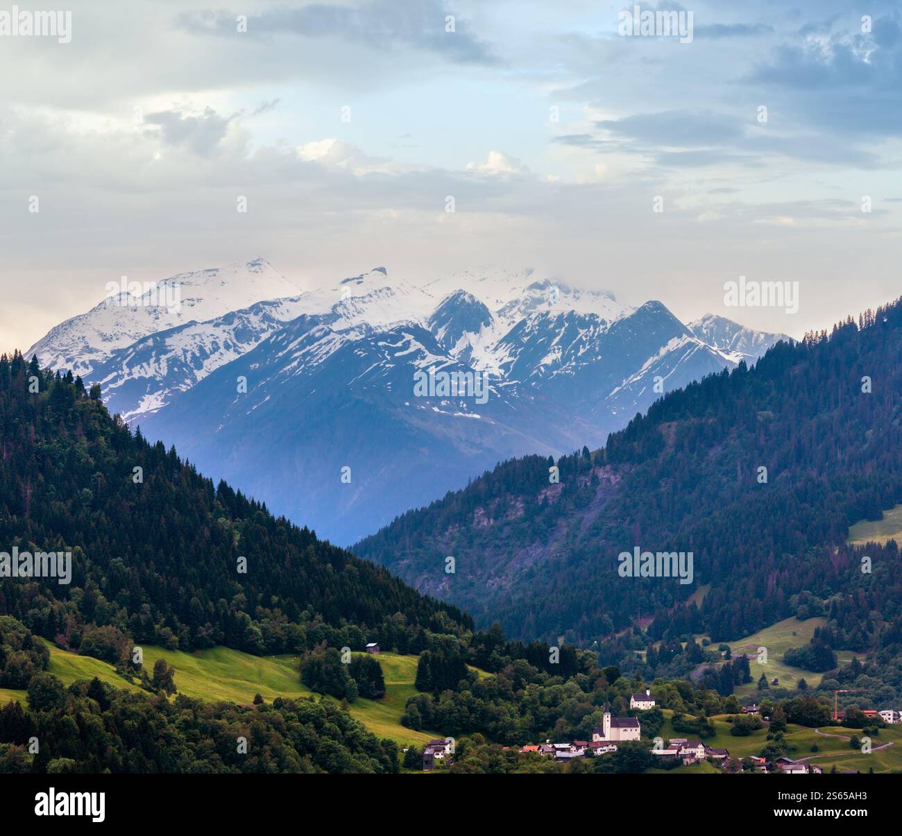 Sommer Alpen Berglandschaft mit Dorf, Tanne Wald am Hang und schneebedeckten Rocky tops in weit, Österreich. Stockfoto