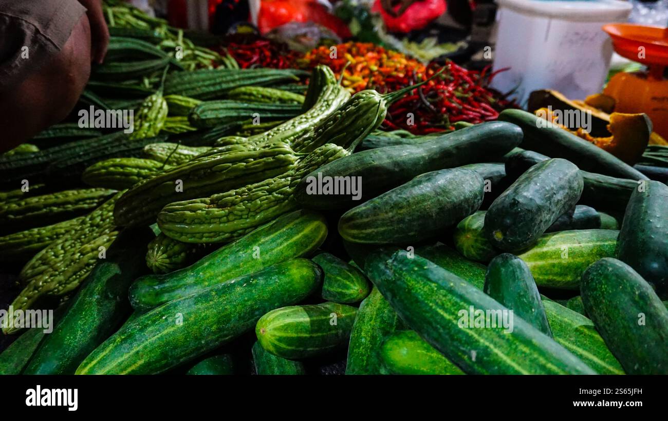 Eine lebhafte Präsentation von frischem Gemüse auf einem Markt mit grünen Gurken und Bitterkürzeln, umgeben von farbenfrohen Chili-Paprika und anderen Produkten Stockfoto