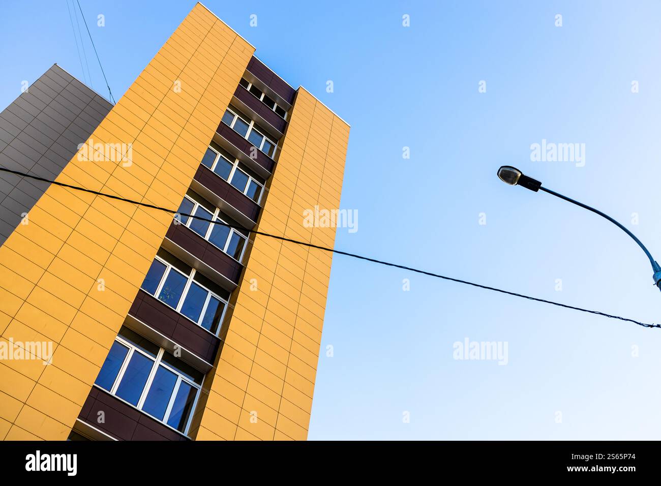 Blick von unten auf die Fassade eines mehrstöckigen Gebäudes, das mit gelben Fliesen gesäumt ist, Stadtlampe mit Elektrodraht und blauem Herbsthimmel im Hintergrund Stockfoto