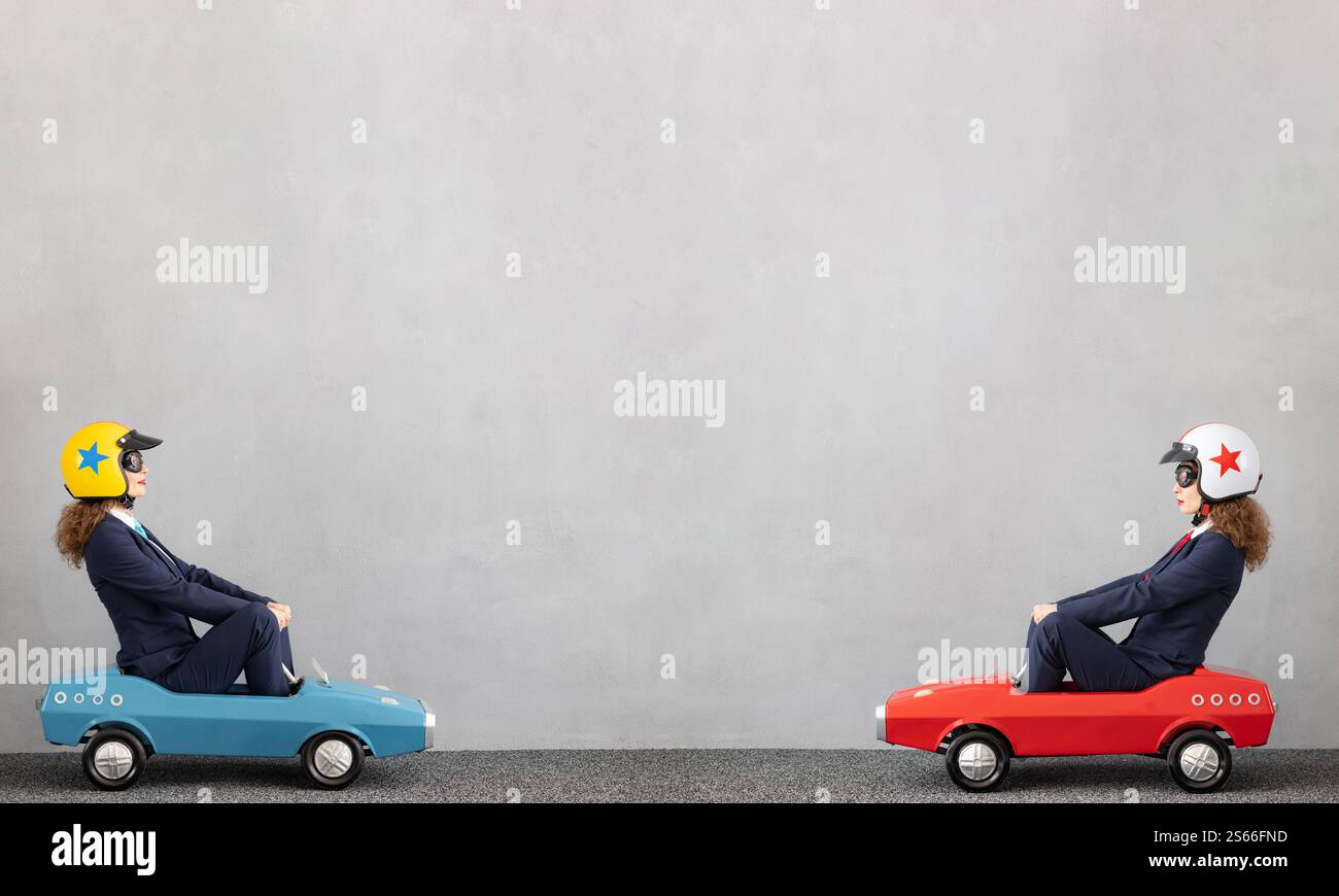 Erfolgreiche Geschäftsfrauen, die im Freien ein Spielzeugauto fahren. Lustige junge Frau vor Betonmauerhintergrund. Business-Srart und Siegerkonzept Stockfoto