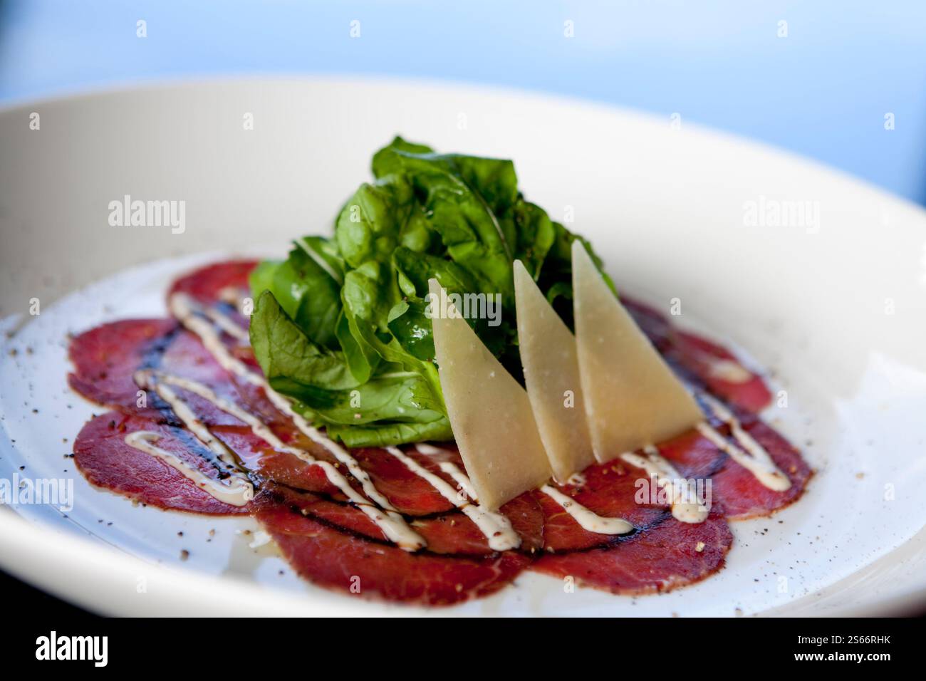 In Scheiben geschnittener roher Rindercarpaccio Rucola-Salat mit Parmesan. Carpaccio ist dünn geschnittenes oder zerstampftes Fleisch und wurde in Venedig, Italien, hergestellt. Stockfoto