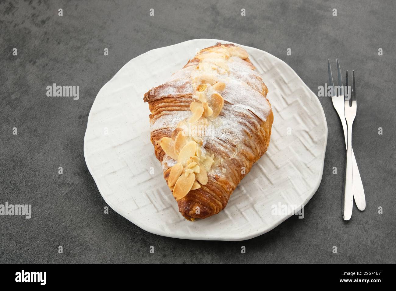 Mandelcroissant mit Puderzucker auf weißem Teller Stockfoto