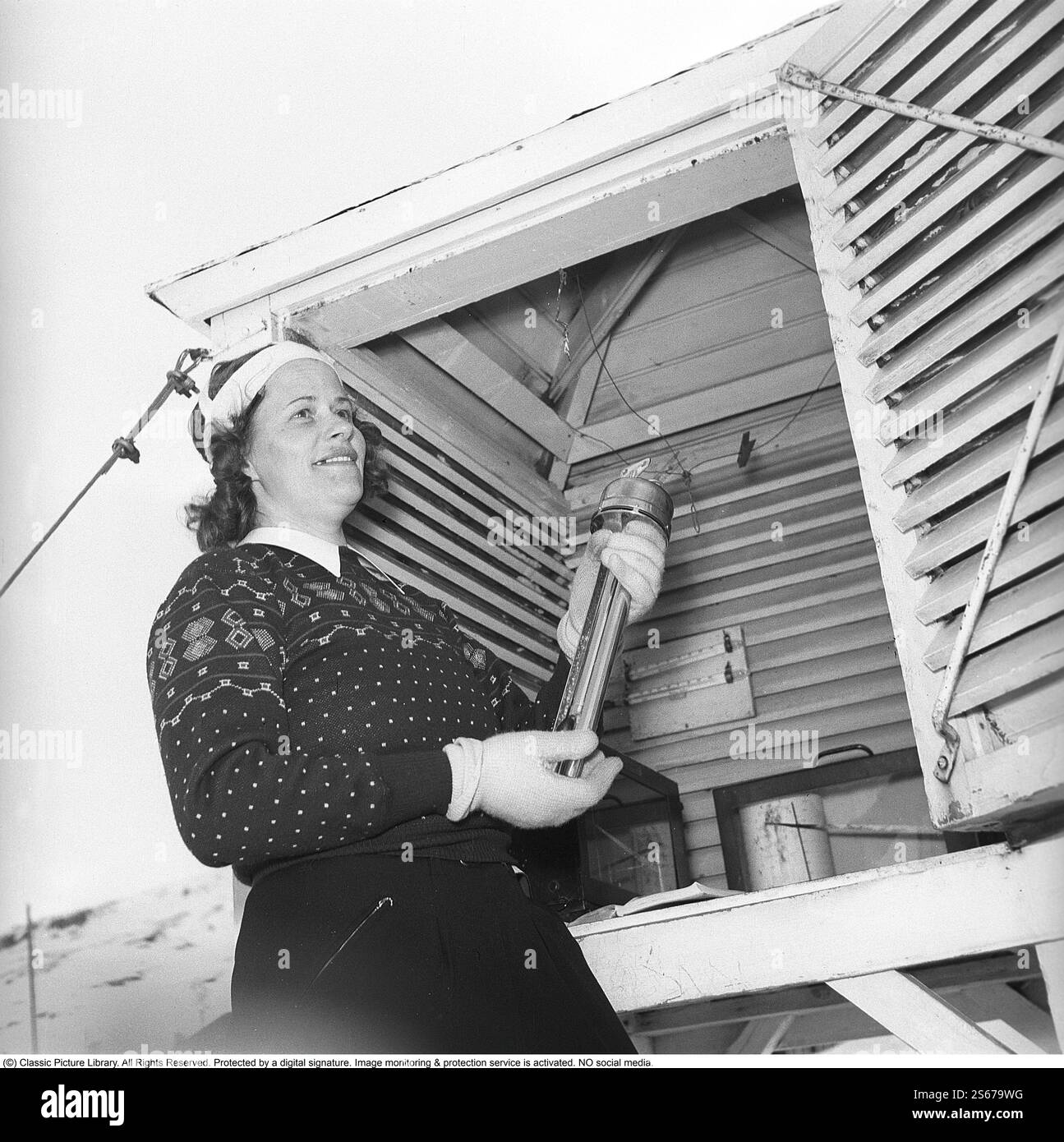 Sie, die das Wetter in den Bergen verfolgt. Es ist die Wetterbeobachterin Anna-Lisa Wikdahl in Riksgränsen in Nordschweden, die sechsmal am Tag ihre Messungen macht und die Instrumente liest. Anschließend ruft sie die Ergebnisse an den Wetterdienst in Stockholm. Hier handhabt sie die Instrumente zur Messung von Temperatur, Niederschlag usw. 1943 Kristoffersson Ref. D107-1 Stockfoto