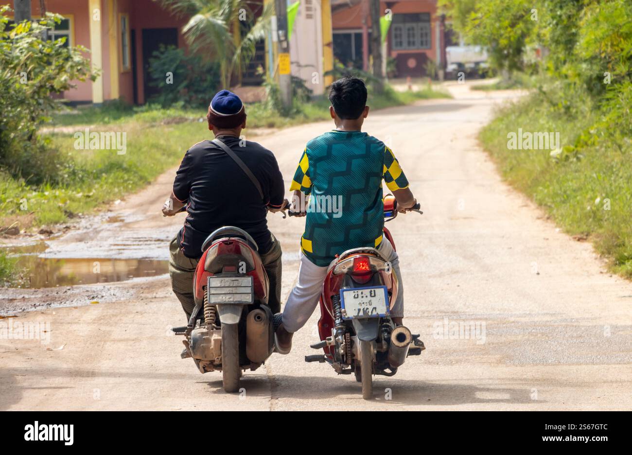 Ein Motorradfahrer schiebt ein anderes Motorrad mit dem Fuß, während er in Thailand fährt Stockfoto
