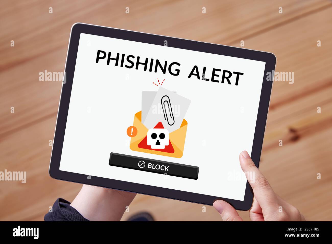 Phishing-Benachrichtigung, die auf einem Tablet angezeigt wird, das von den Händen einer Frau zu Hause gehalten wird und Online-Betrugswarnungen symbolisiert. Stockfoto