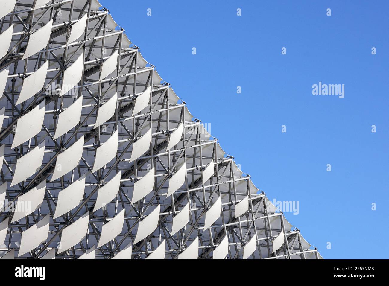 Ein Fragment moderner Architektur – ein Raster aus weißen, diamantförmigen Paneelen, die eine große, abstrakte Oberfläche am Himmel bilden. Stockfoto