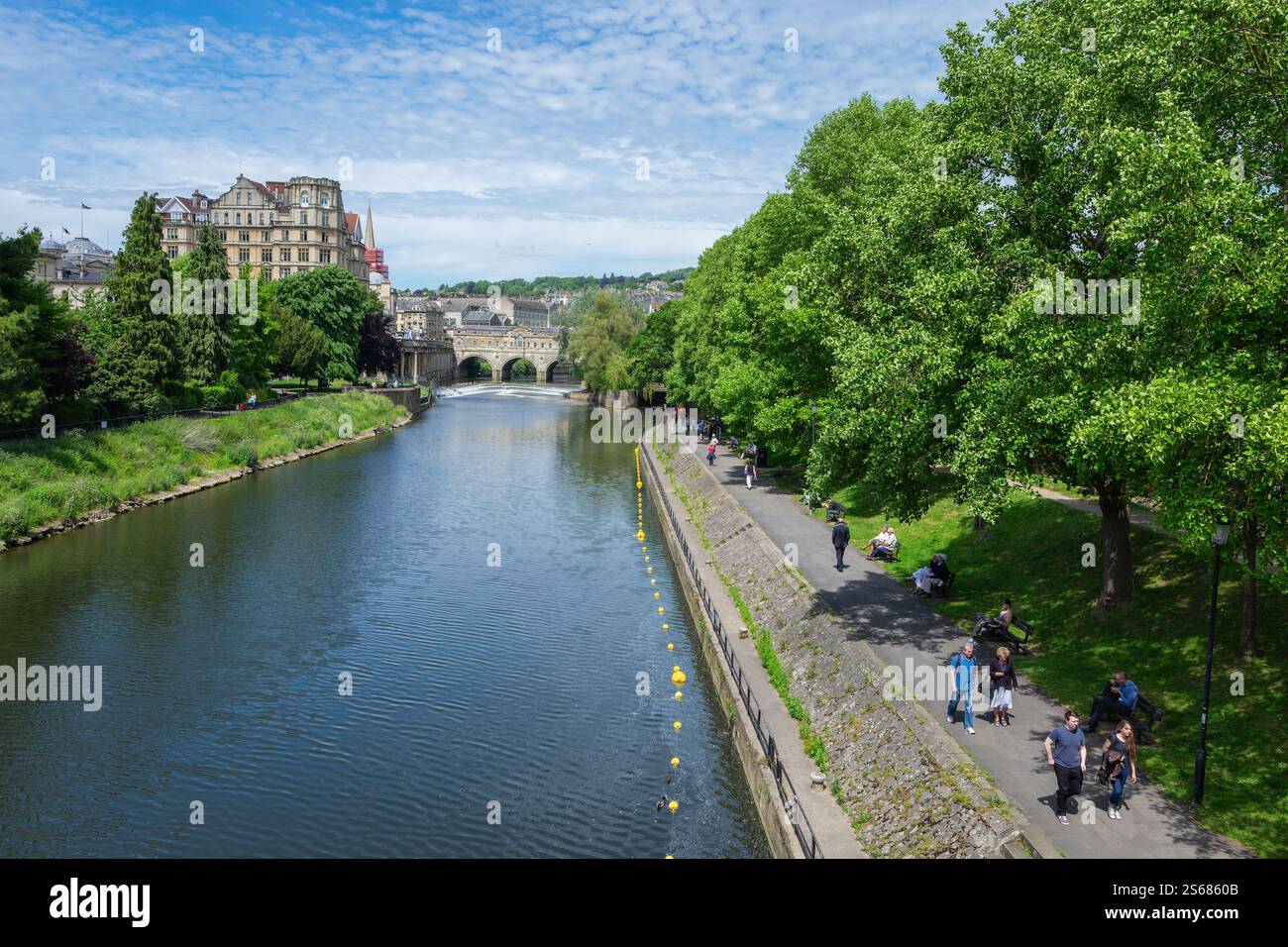 Menschen, die entlang des Flusses Avon in Bath UK spazieren, mit der historischen Pulteney Bridge und dem Empire Hotel, die eine atemberaubende architektonische Kulisse bieten. Stockfoto