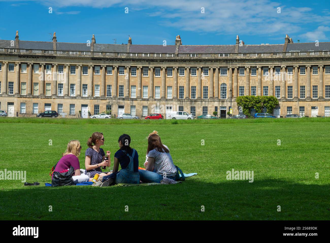 Menschen, die auf dem Gras vor dem Royal Crescent in Bath, Großbritannien sitzen, genießen das warme Wetter, die malerische Aussicht und die historische georgianische Architektur. Stockfoto