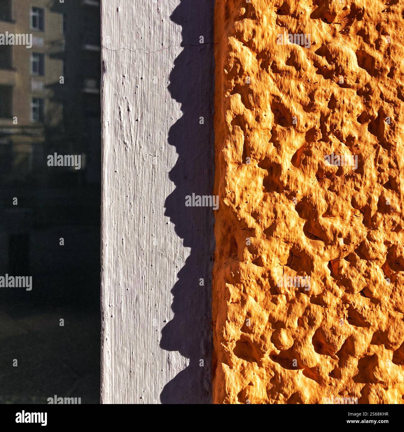 Detaillierte Ansicht einer leuchtend orange strukturierten Wandoberfläche im Kontrast zu den Schatten im Sonnenlicht. Mit architektonischen Details. - Smartphone-aufgenommenes Stockfoto