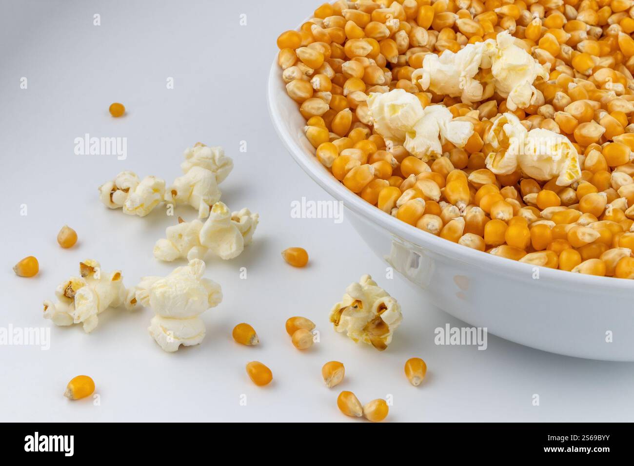 Mais für Popcorn. Teller mit Maiskernen auf weißem Hintergrund. Imbiss im Kino. Stockfoto