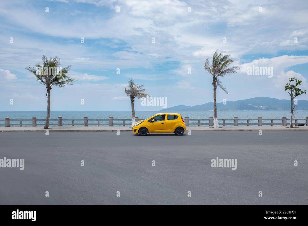 Auto fährt auf der Straße am Meer. Gelbes Auto, das auf einer Küstenstraße mit Palmen und blauem Himmel fährt. Transport, Reisen, Urlaub Stockfoto