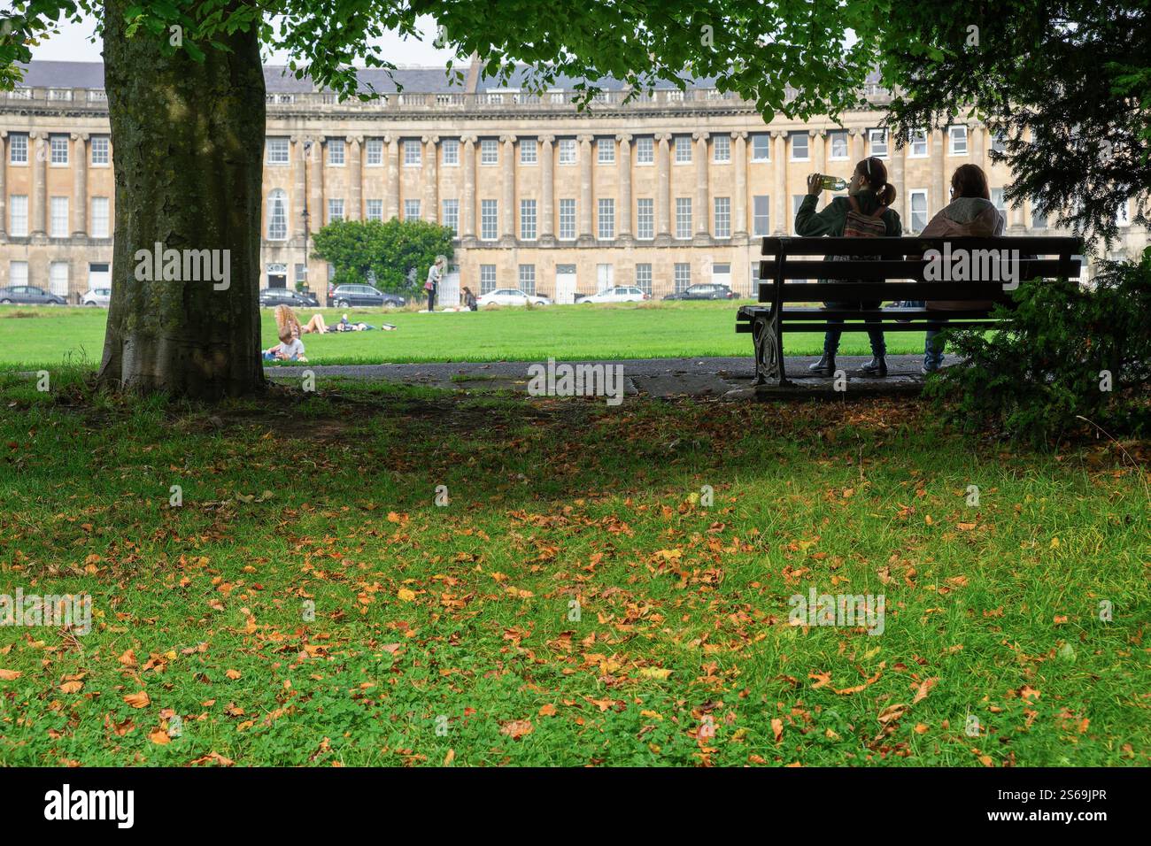 Die Menschen sitzen auf einer Bank vor dem historischen Circus in Bath, Großbritannien, umgeben von georgianischer Architektur und einer friedlichen urbanen Umgebung. Stockfoto