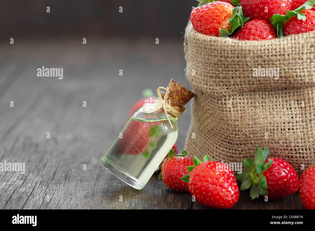 Glasflasche mit ätherischem Erdbeeröl mit frischen Erdbeeren auf Holztisch, alternative Medizin ( Fragaria ) Stockfoto