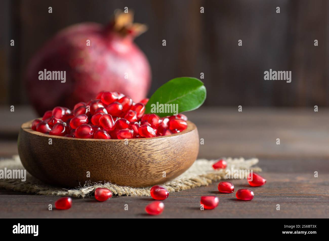 Frischer reifer ganzer und gespaltener saftiger Granatapfel mit Samen und Blättern auf rustikalem hölzernem Hintergrund, gesunde rote Früchte Konzept Kopierraum (Punica granatum Stockfoto