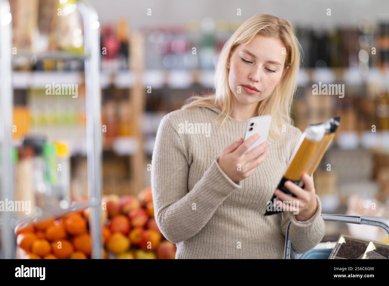 Prüfen des Ablaufdatums von Spaghetti – weibliche Käuferinnen scannen den QR-Code auf dem Etikett von Spaghetti mit Smartphone Stockfoto