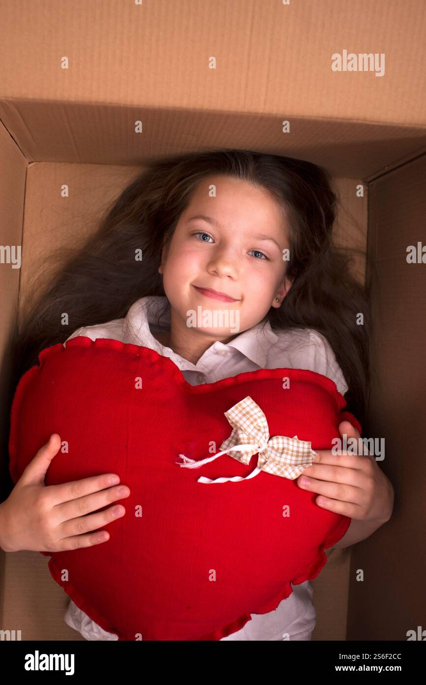 Lächelndes Kind, das in der Schachtel liegt, mit großem rotem Herzen Stockfoto