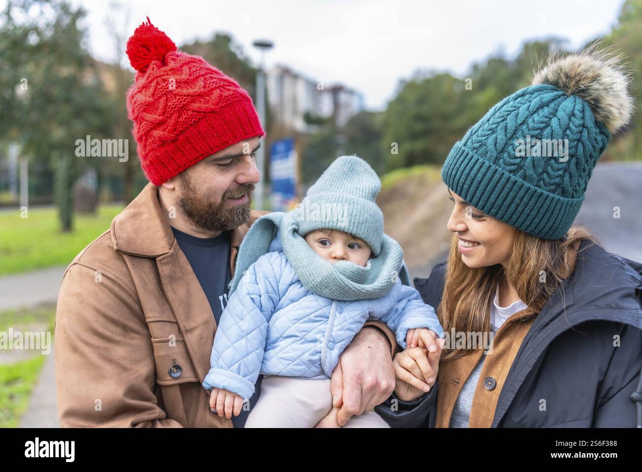 Eltern halten ihr Baby in der Hand, während sie im Winter einen gemütlichen Spaziergang durch einen Park machen, der eine herzerwärmende Szene der Familienbindung schafft Stockfoto Eltern halten ihr Baby in der Hand, während sie im Winter einen gemütlichen Spaziergang durch einen Park machen, der eine herzerwärmende Szene der Familienbindung schafft Stockfoto