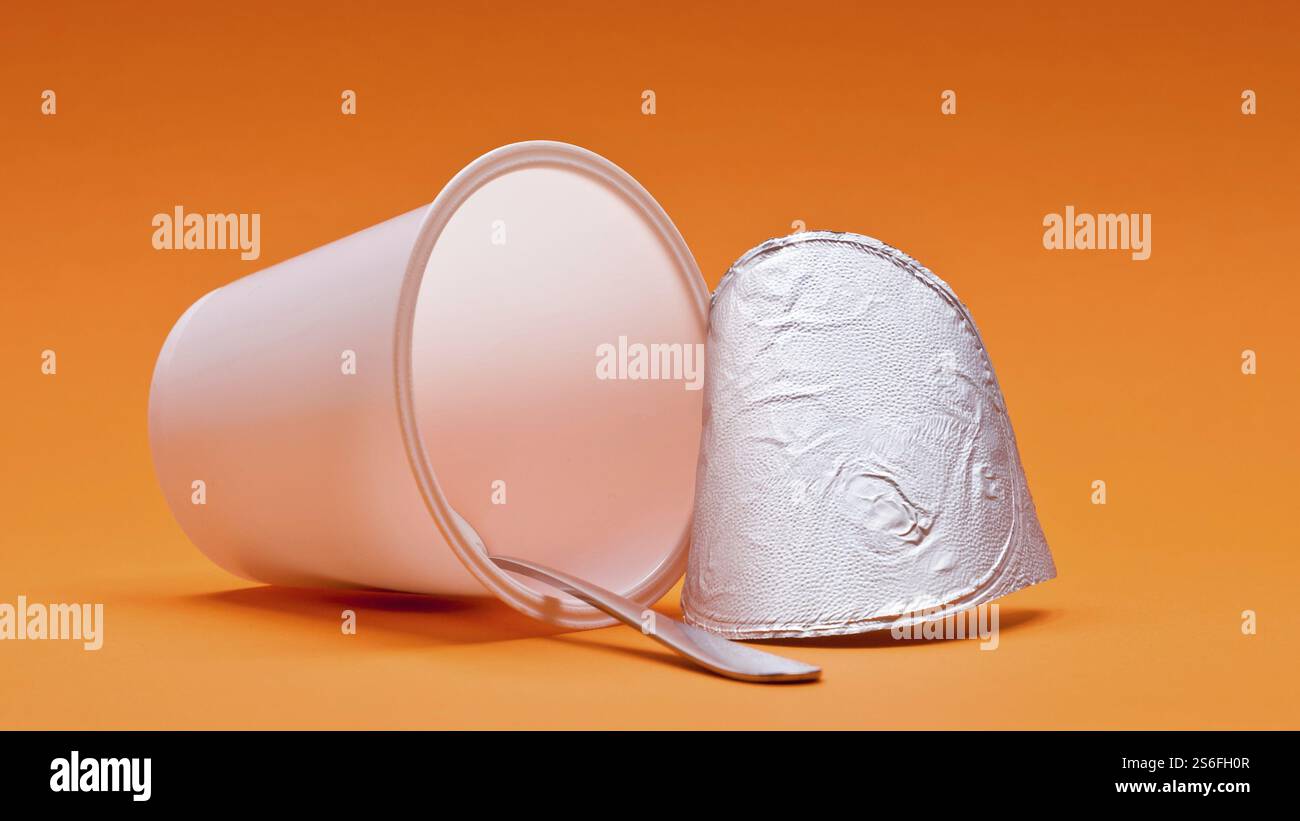 Ein leerer, sauberer Joghurtbecher mit Löffel auf orangem Hintergrund Stockfoto