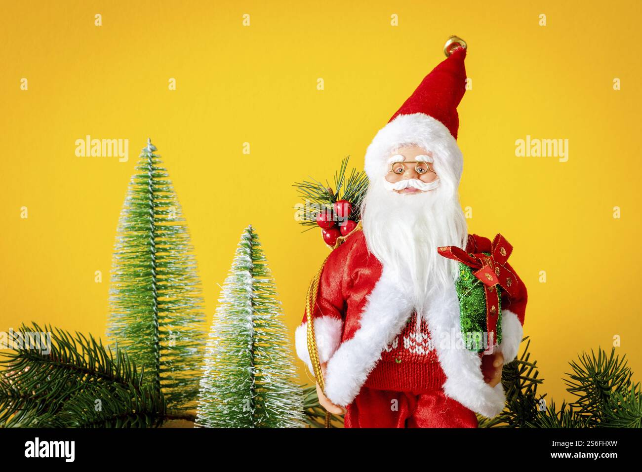 Eine Weihnachtsmann-Figur mit Tannenbäumen auf gelbem Hintergrund Stockfoto