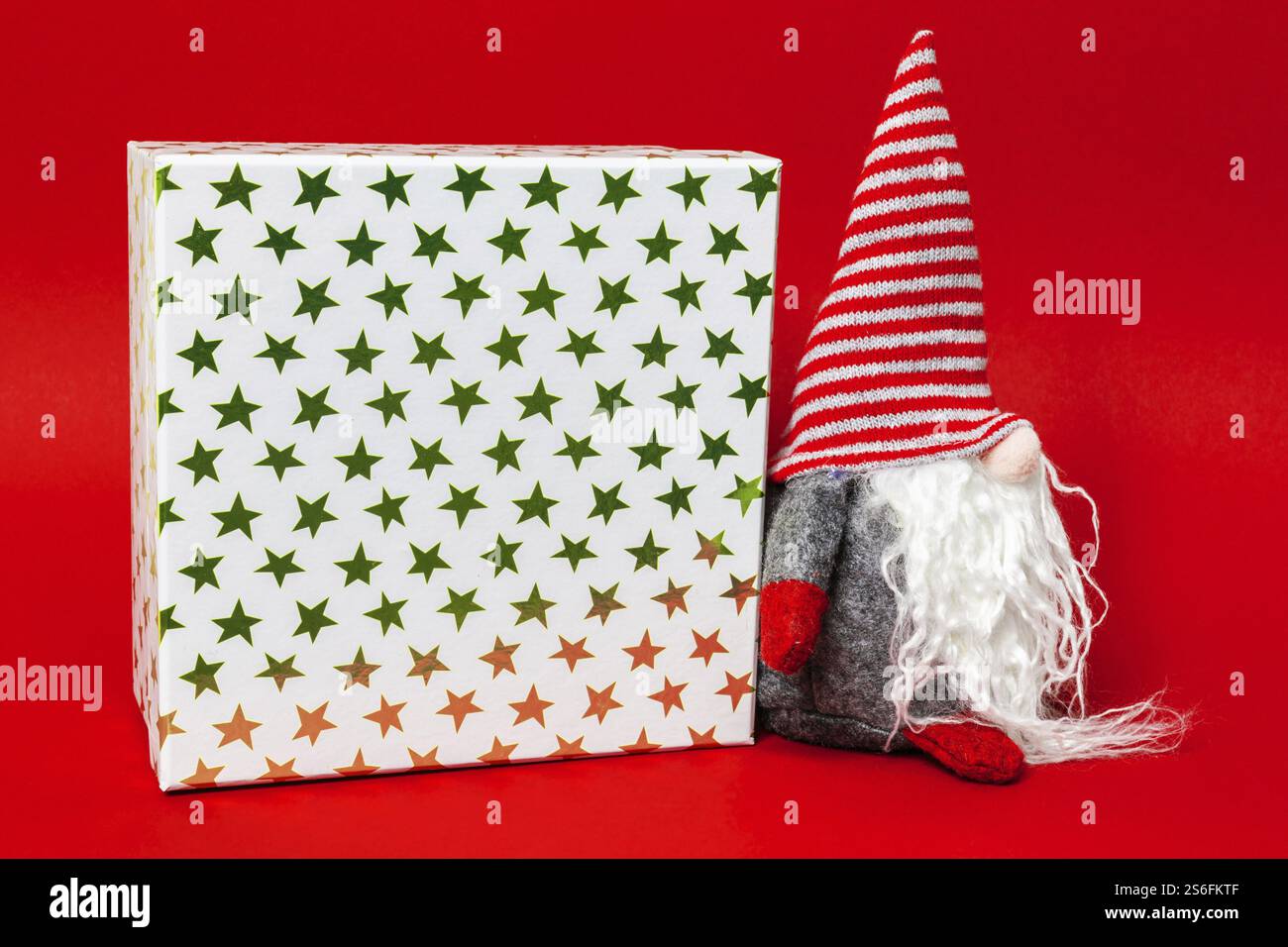 Weihnachtsdekoration mit einem gnome und einem Geschenkkarton auf rotem Hintergrund Stockfoto