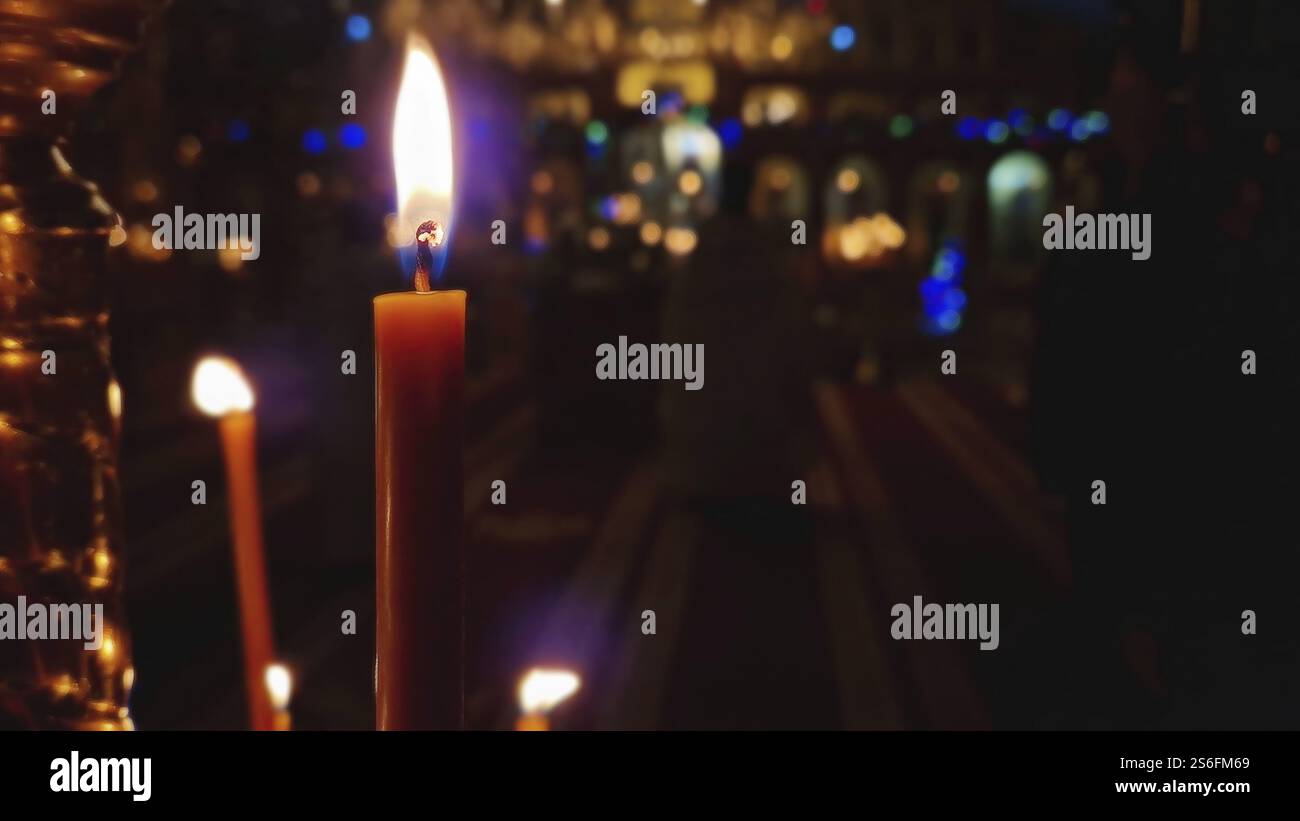 Nahaufnahme einer brennenden Kerze auf dem Kerzenhalter in einer christlich-orthodoxen Kirche. Die brennende Flamme ist scharf und hell. Religiöses Symbol für Ostern oder C. Stockfoto