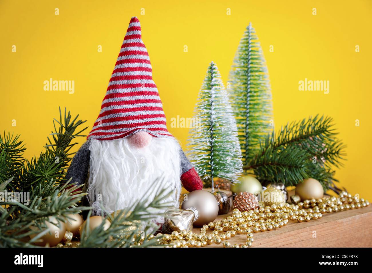 Eine Weihnachtsdekoration mit einem Zwerg auf einer Holzkiste und gelbem Hintergrund Stockfoto