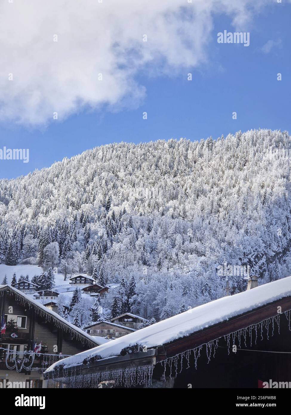 Idyllische Winterszene mit schneebedecktem Dorf La Clusaz, eingebettet in eine hügelige Landschaft, Annecy, Frankreich. Holzhäuser verstreut über den schneebedeckten Hügel Stockfoto