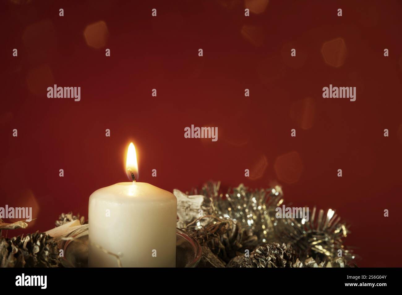 Weihnachtsdekoration mit einer brennenden Kerze auf rotem Hintergrund Stockfoto