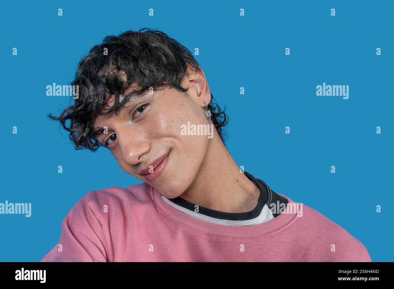 Porträt eines fröhlichen jungen Mannes mit lockigen Haaren und rosa Sweatshirt, das auf einem leuchtend blauen Hintergrund posiert Stockfoto