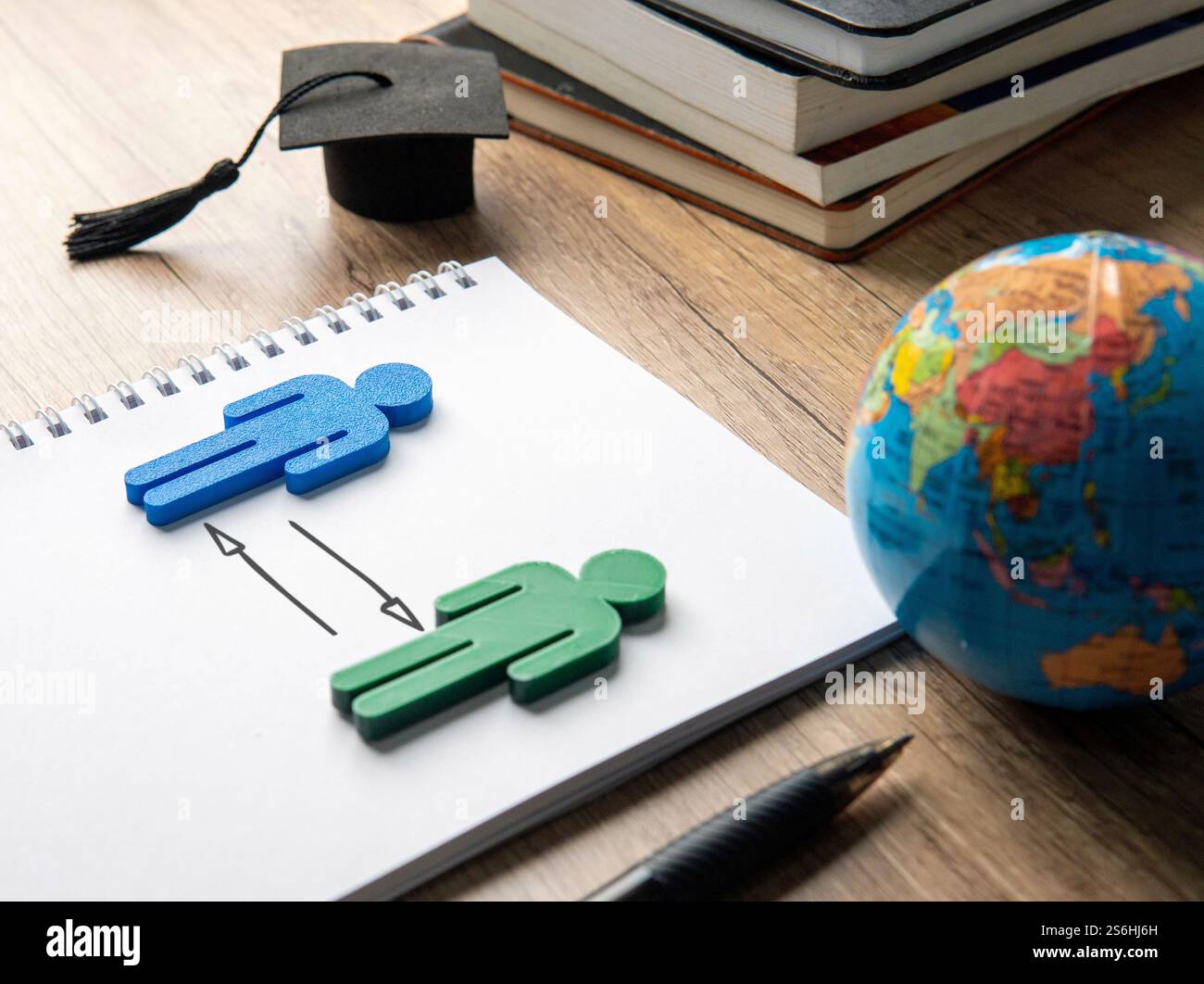 Eine Graduierungskappe, eine Kugel und zwei Figuren mit Pfeilsymbol. Bildung, Internationales Studium und Austauschstudienkonzept. Stockfoto