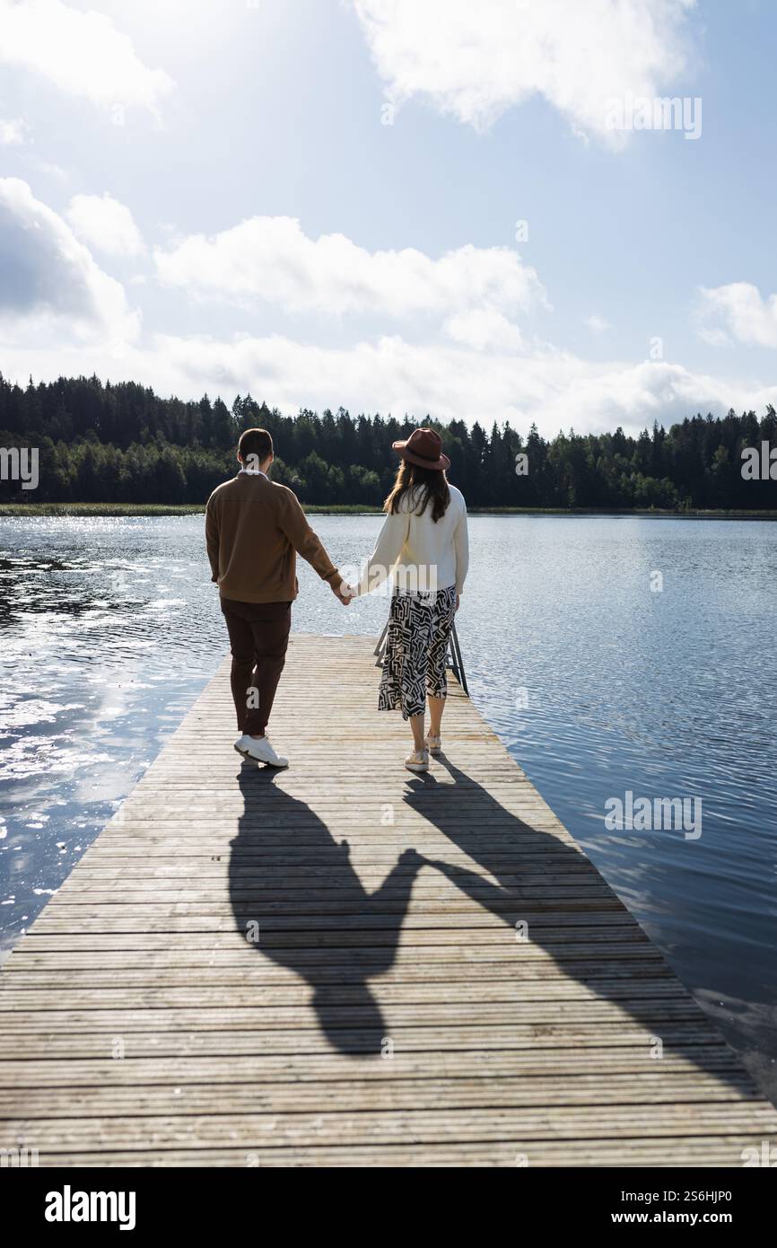 Junges erwachsenes Paar, das auf dem Pier am See läuft und Hände hält Stockfoto