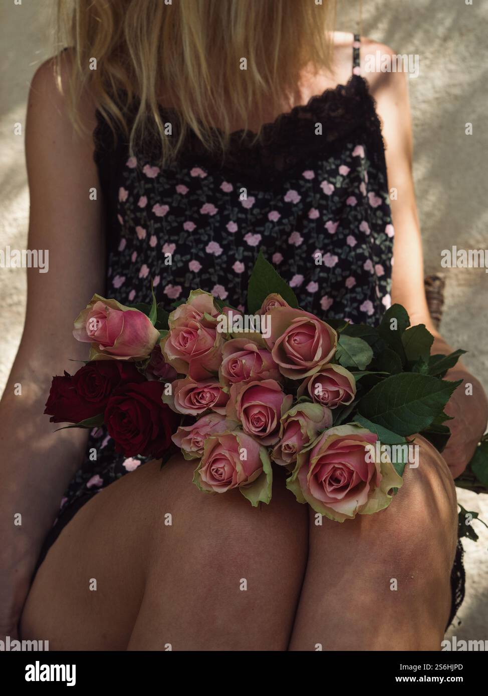 Seidenbekleidete Frau mit Teerosen auf Lap auf italienischer Veranda, gesichtslos Stockfoto