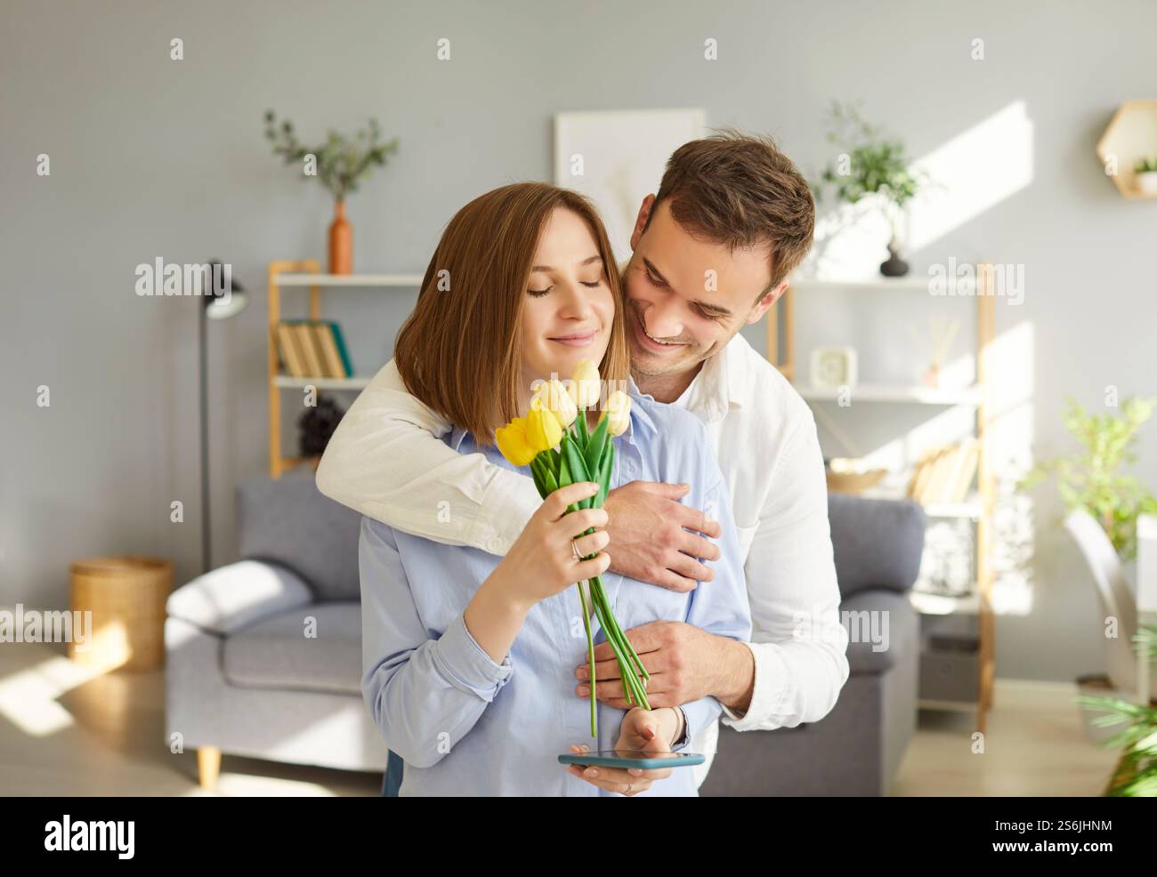 Der liebende Ehemann umarmt seine Frau mit einem Tulpenstrauß, feiert den Frauentag oder Geburtstag zu Hause. Stockfoto Der liebende Ehemann umarmt seine Frau mit einem Tulpenstrauß, feiert den Frauentag oder Geburtstag zu Hause. Stockfoto