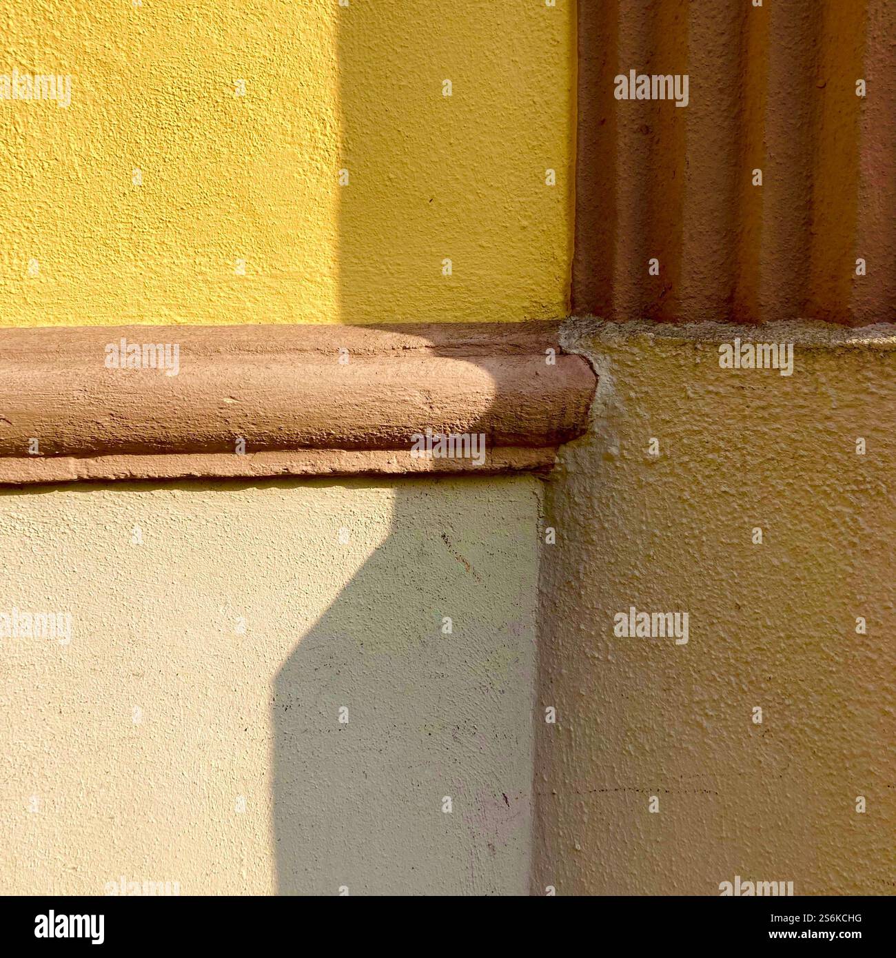 Nahaufnahme einer Wandecke im Freien mit gelben und beigefarbenen Farben unter Sonnenlicht, die Textur und Struktur betonen. - Smartphone-aufgenommenes Stockfoto