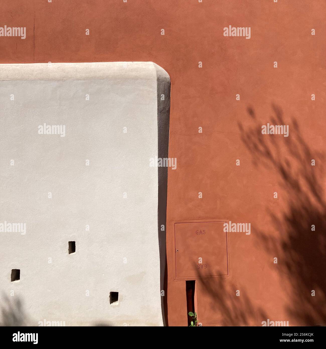 Sonnenlicht blickt über eine Stuckwand mit weißen und terrakottafarbenen Kontrasten und Schattenstrukturen. - Smartphone-aufgenommenes Stockfoto